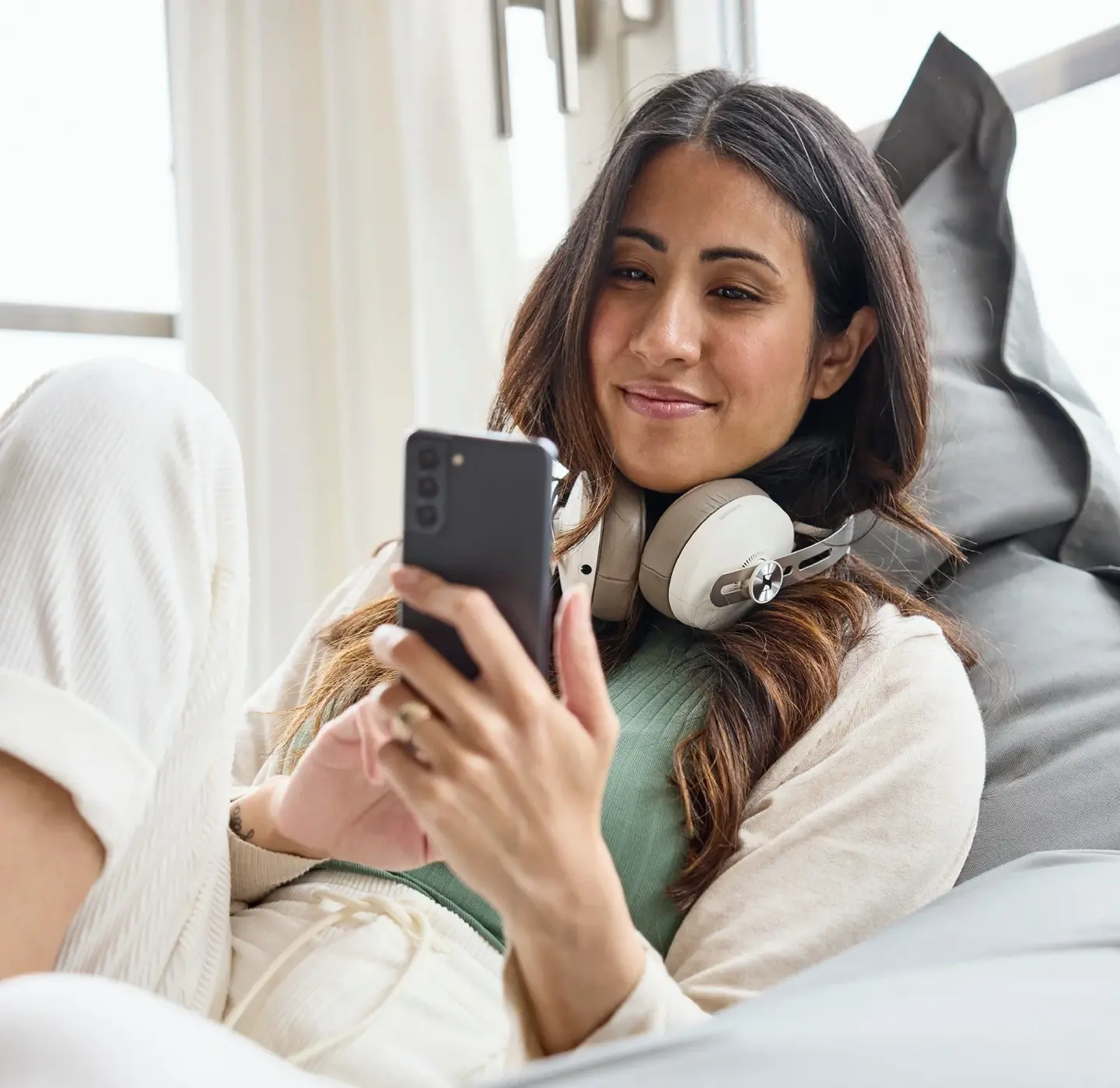 Frau mit Kopfhörern entspannt auf einem Sitzsack und nutzt ein Smartphone.