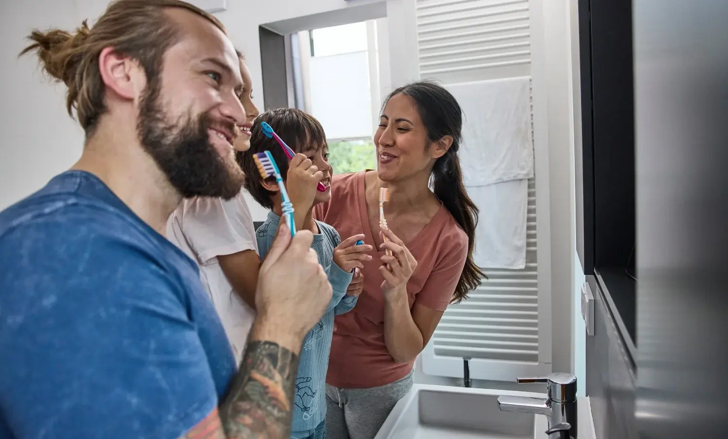 Ein Vater steht mit seiner Frau und seinen zwei Kindern im Bad vor dem Spiegel und putzt seine Zähne.