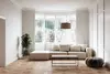 Helles Wohnzimmer mit beigem Sofa, Tisch und Stehlampe, sowie einer Pflanze in der Ecke.