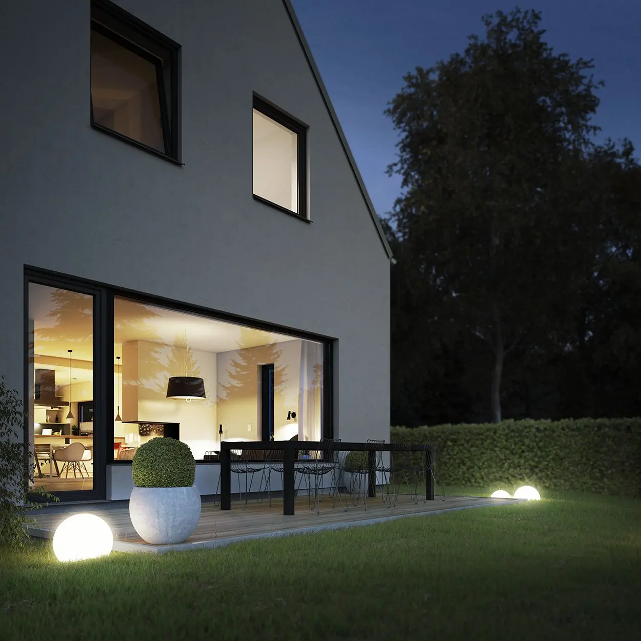 Moderne Terrasse mit runden Gartenleuchten, einem Tisch und Stühlen vor einem Wohnhaus bei Nacht.