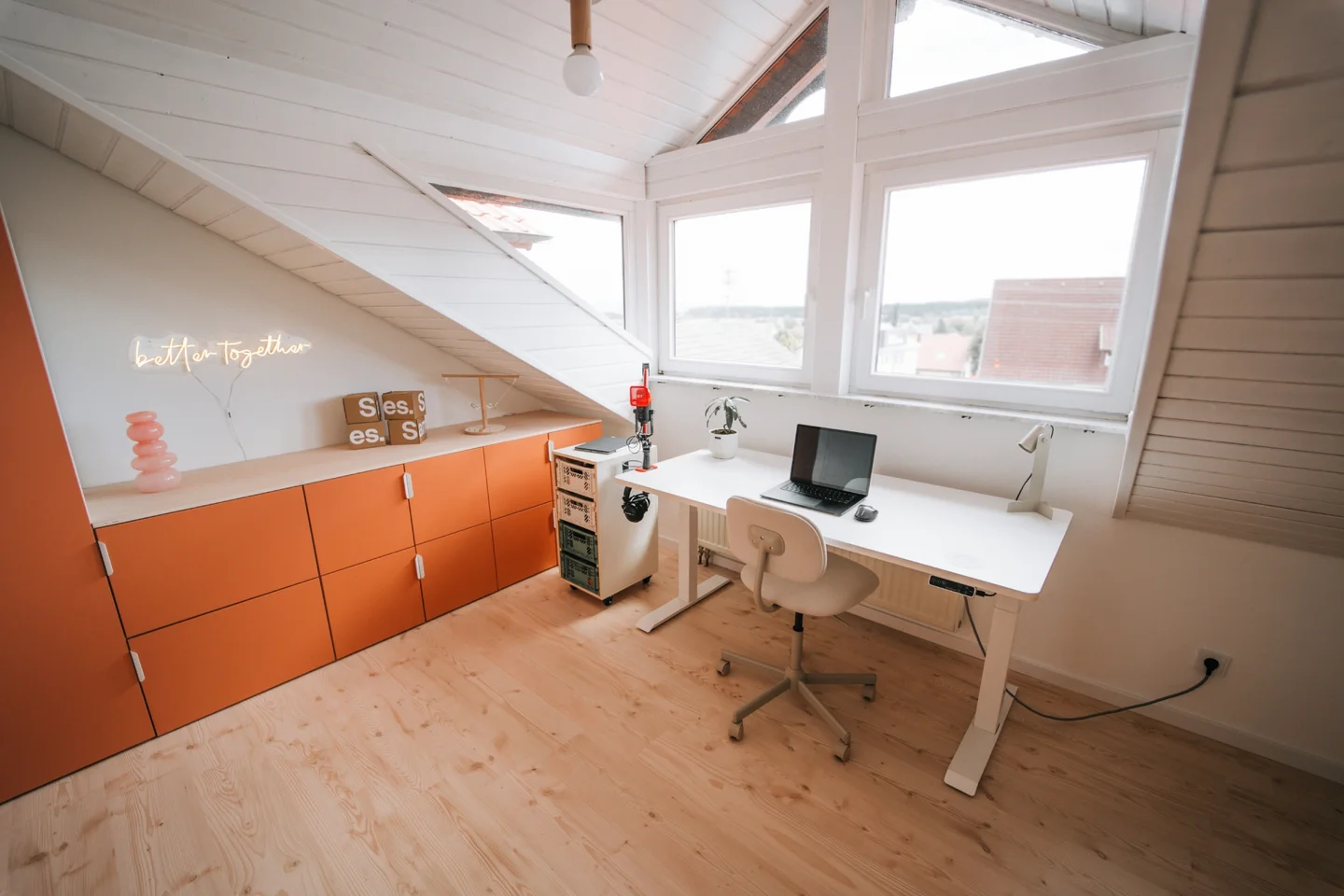 Dachgeschosszimmer mit Fenster, das als Home Office genutzt wird. Ausgestattet mit orangener Schrankwand und weißem Schreibtisch.