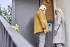 Zwei ältere Personen stehen an einer Eingangstür und betrachten ein Haustelefon oder eine Gegensprechanlage.