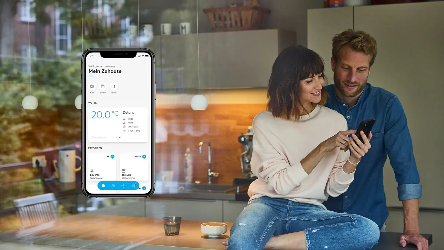 Smartphone displaying a smart home app, with a couple reviewing it together in a kitchen setting.