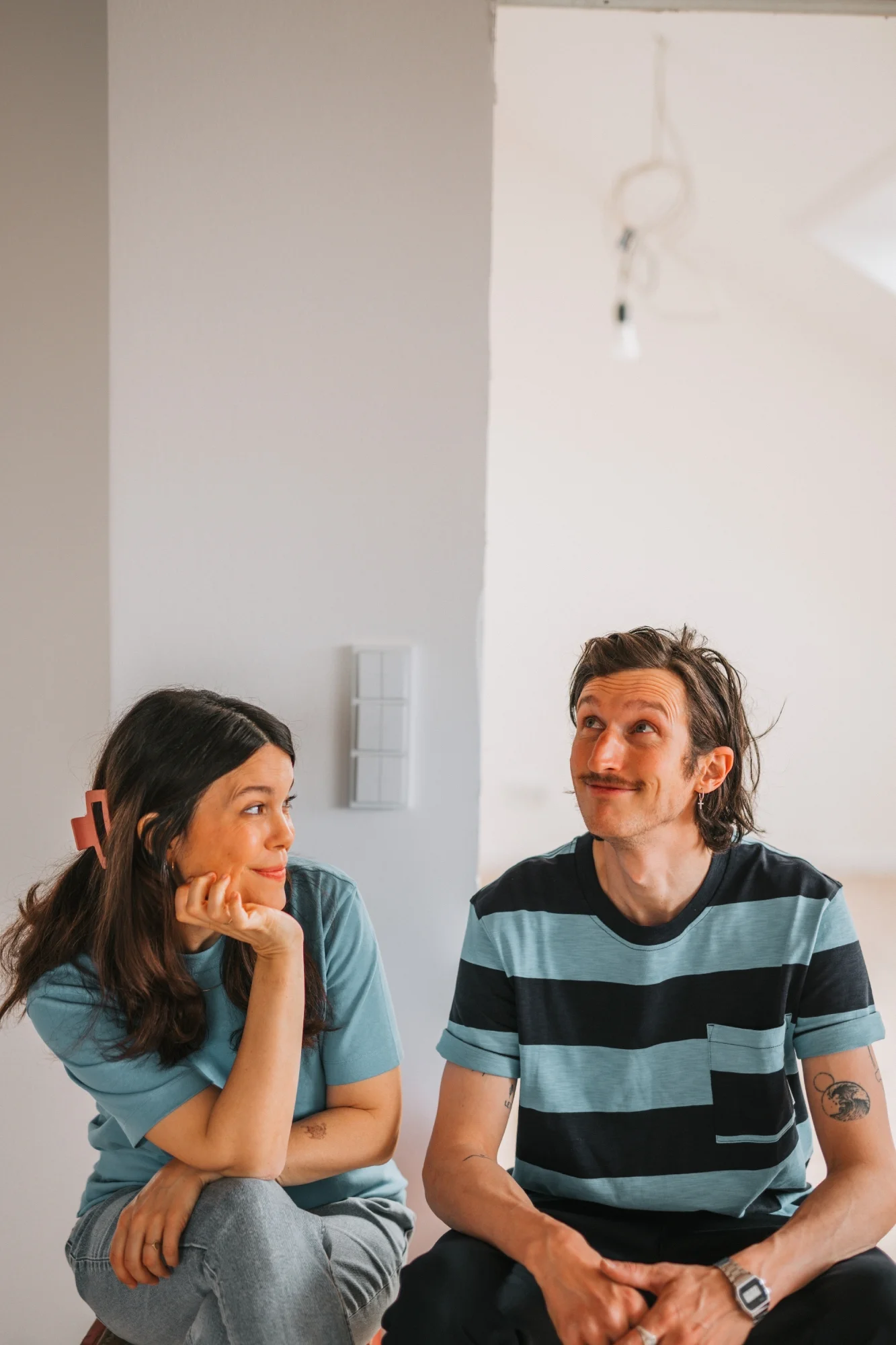 Ein Paar sitzt schmunzelnd vor einer Wand - im Hintergrund sind Smart Home Lichtschalter zu erkennen.