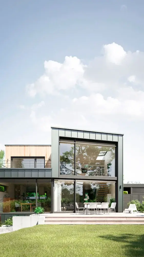 Moderne zweigeschossige Wohnhausfassade mit großen Fenstern und Terrasse, umgeben von Rasen und Pflanzen.