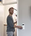 Mann steht an einer geöffneten Tür und greift nach einem Bedienfeld an der Wand.